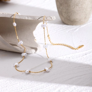Elegant gold chain necklace with irregular white pearls on a light stone textured surface