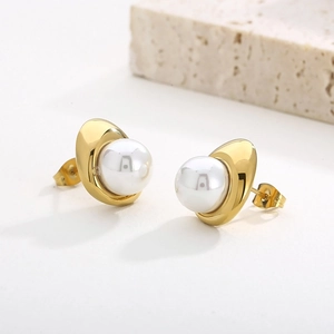 Detail view of gold C-shaped earrings with white pearl inlay on textured stone background