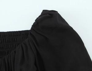 Gros plan sur la texture smockée noire et les manches bouffantes du chemisier