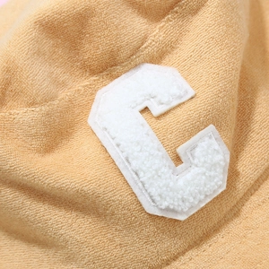 Nahaufnahme gelber Fischerhut aus Frottee mit weißem Chenille-Buchstaben C-Aufnäher