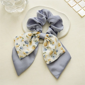 Detailed view of gray-blue floral double-layered bow hair tie on a minimalist beige mat