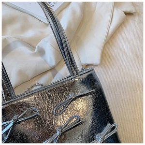 Detail of silver metallic handbag featuring four matching decorative bow ties on the surface