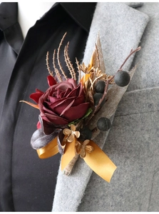 Nahaufnahme einer burgunderroten Kunstrose-Ansteckblume mit Goldblättern auf grauem Sakko