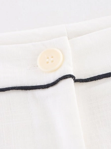 Detailed macro view of cream linen trousers with button closure and black piping detail