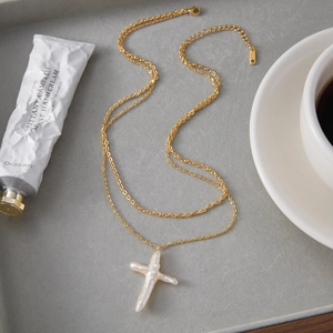 Baroque pearl cross pendant necklace displayed with coffee in a lifestyle setting