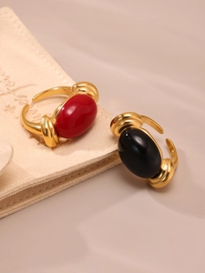 Detail of 18k gold plated open rings with red and black resin stones on beige fabric