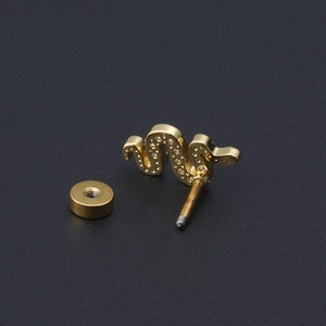 Macro shot of gold snake earring with zircon crystals on a black matte surface