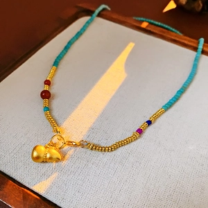 Close-up of gold-plated gourd necklace with turquoise and colored beads on wood tray