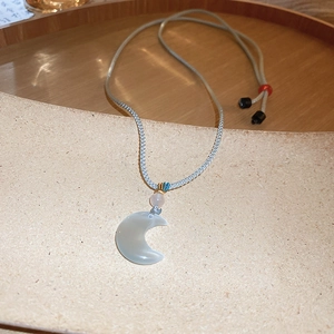 Detail of sun and moon pendant necklace featuring light blue crescent and pink bead charm