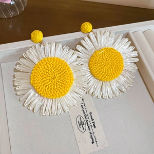 Detail of woven daisy earrings with white petals and yellow centers in French style