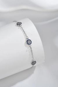 Macro shot of silver evil eye bracelet with blue and white zircon on silk background