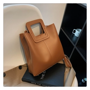 Dettaglio di una borsa a secchiello in pelle marrone con manico vuoto su sedia e trench