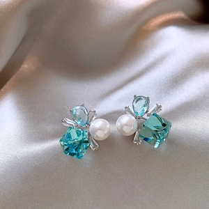 Primo piano di orecchini geometrici con zircone blu e perle su seta color champagne