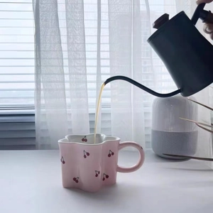 Pink ceramic cherry mug with wavy edge being filled with coffee in a cozy home setting
