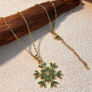 Collana dorata in acciaio con pendente a fiocco di neve verde su un ramo rustico