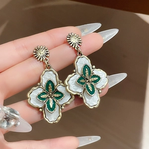 Gros plan de boucles d'oreilles fleur vintage en or avec nacre blanche et émail vert