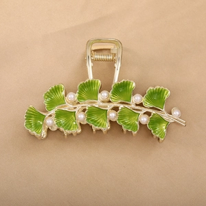Elegante gouden ginkgo haarklem met groen email en witte parels op stoffen achtergrond