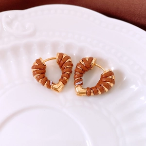 Macro view of heart-shaped 18k gold earrings with brown leather winding on a white tray