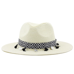 Détail d'un chapeau de paille beige avec ruban à pompons et breloques de pièces