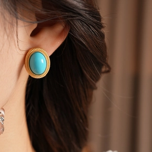 Close-up of vintage oval turquoise earrings with textured gold border worn by a model
