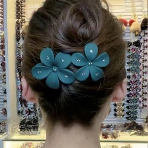Detail view of a person wearing two dark green floral hair clips with sparkling rhinestones