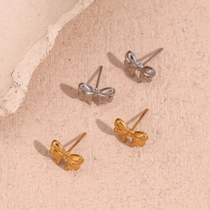 Detailed close-up of gold and silver bow stud earrings on a minimalist stone background