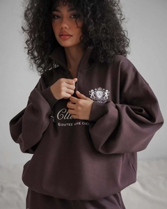 Détail d'un sweat marron à quart de zip avec imprimé Club et broderie blason de lion