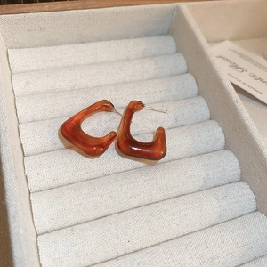 Detailed close-up of amber resin geometric C-shape earrings on a white jewelry display