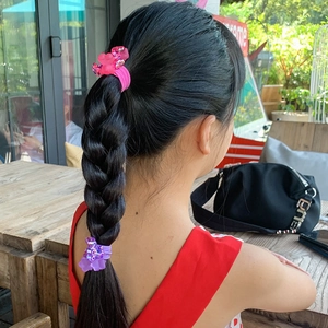 Pink and purple flower hair ties used on braided hair for girls in outdoor setting