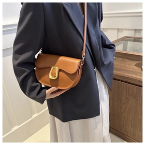 Close-up of brown leather saddle bag featuring a decorative gold horseshoe metal buckle