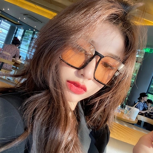Detail of square vintage sunglasses with translucent orange lenses worn in cafe setting