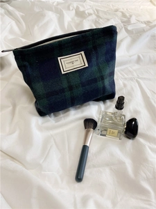 Detail of plaid cosmetic bag with Pleasant Time label next to perfumes and brushes
