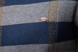 Gros plan sur la maille rayée bleue et grise du pull avec logo en métal