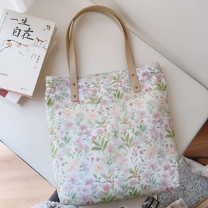 Flat lay of floral canvas tote bag with leather straps next to a cat-themed book