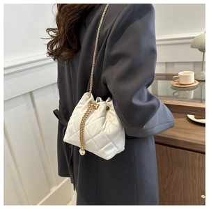 Detail of white quilted bucket bag featuring a gold chain and elegant pearl drawstring