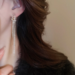 Detail view of heart-shaped knot earrings with sparkling rhinestone tassels on model