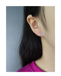 Close-up of a silver heart-shaped knot stud earring worn by a female model