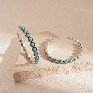 Detail of silver hoop earrings with turquoise beads on textured stone surface