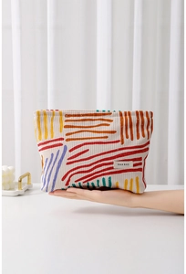 Detail of floral corduroy makeup bag showing colorful abstract stripes and brand label