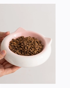 Close-up of pink and white ceramic cat-ear shaped pet bowl being held by hand with dry food