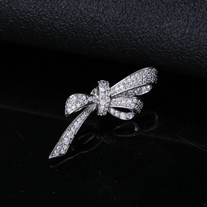 Macro shot of silver bow brooch featuring micro-set zircon on black reflective surface