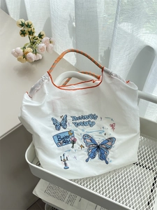 Detail of white embroidered tote bag featuring a blue butterfly and woven rope handles