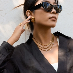 Détail de colliers multicouches en acier titane doré et boucles d'oreilles sur mannequin