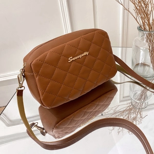 Brown quilted crossbody camera bag with gold hardware shown in a minimalist interior setup