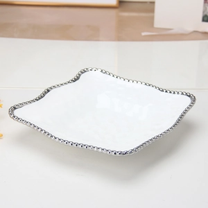 Detailed close-up of a white ceramic plate with silver beaded rim and wavy edges