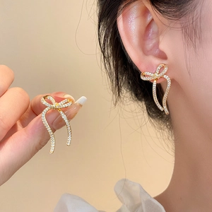 Elegant gold bow earrings with sparkling zircons worn for a luxury jewelry showcase