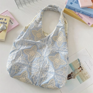 Detail of light blue lace tote bag with white butterfly floral embroidery and ruched handles