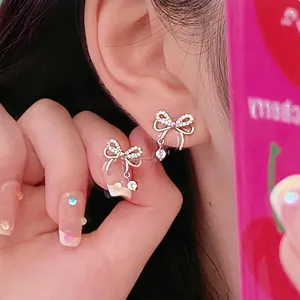 Close-up of silver bow earrings with zircon micro-pave and dangling round crystal studs
