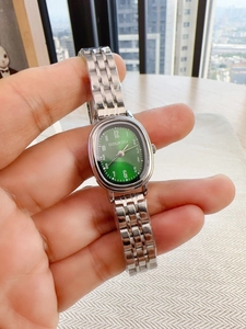 Detail view of oval silver watch with green dial and metal strap worn on the wrist