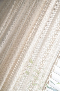 Close-up of beige crochet lace curtain featuring intricate floral patterns and pom-pom trim